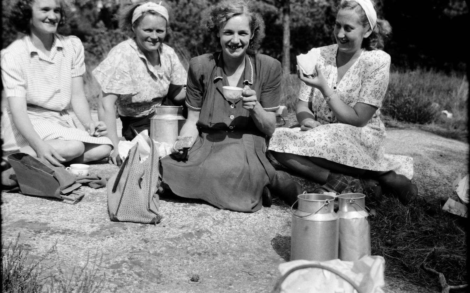 Fyra lingonplockande kvinnor tar en kaffepaus med korvsmörgåsar och mjölk ur stora mjölkkannor.  Platsen är någonstans i Halland. Fotografen Erik ”Kloar-Erik” Andersson var verksam mellan 1930 och 1966. 